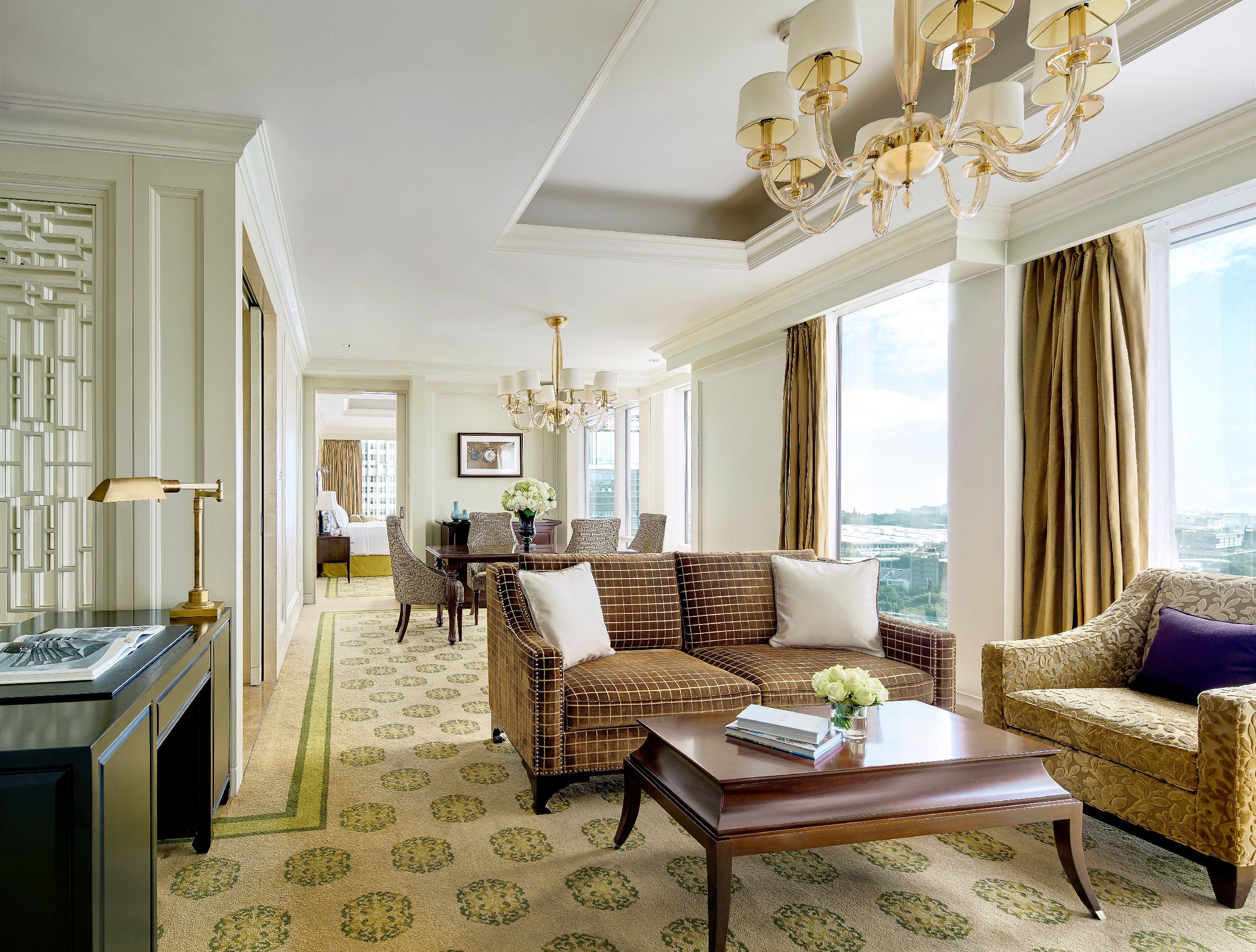 A hotel room with a chandelier, a dining area with a table and chairs, and a view of the city.