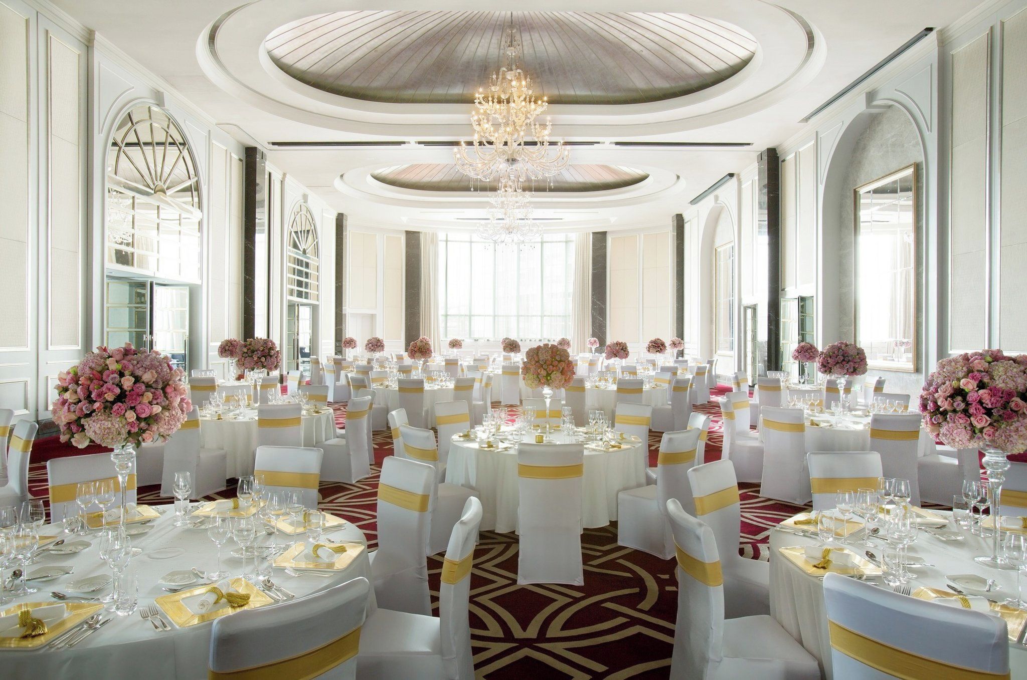 A banquet hall with round tables, white chairs, and floral centerpieces.