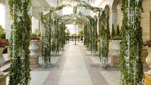 An indoor corridor with a central pathway flanked by white columns and arches adorned with greenery. - The Langham, Shenzhen (Shenzhen)