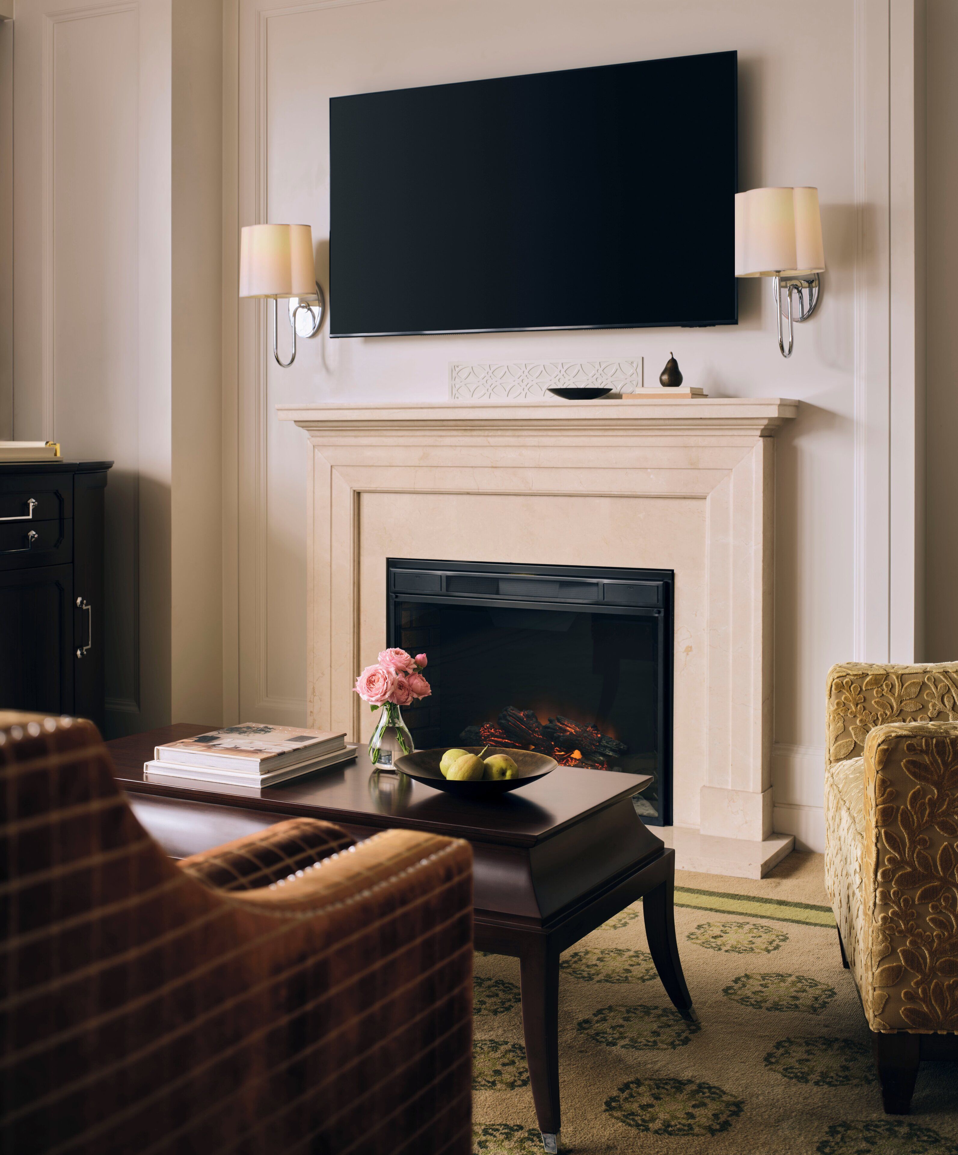 A living room with a fireplace, a flat-screen TV mounted above it, and two wall-mounted lamps.