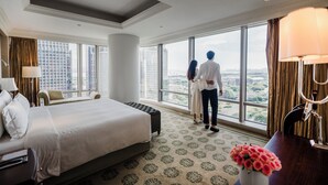 A hotel room with a large bed, a desk, and a view of the city through large windows. - The Langham, Shenzhen (Shenzhen)