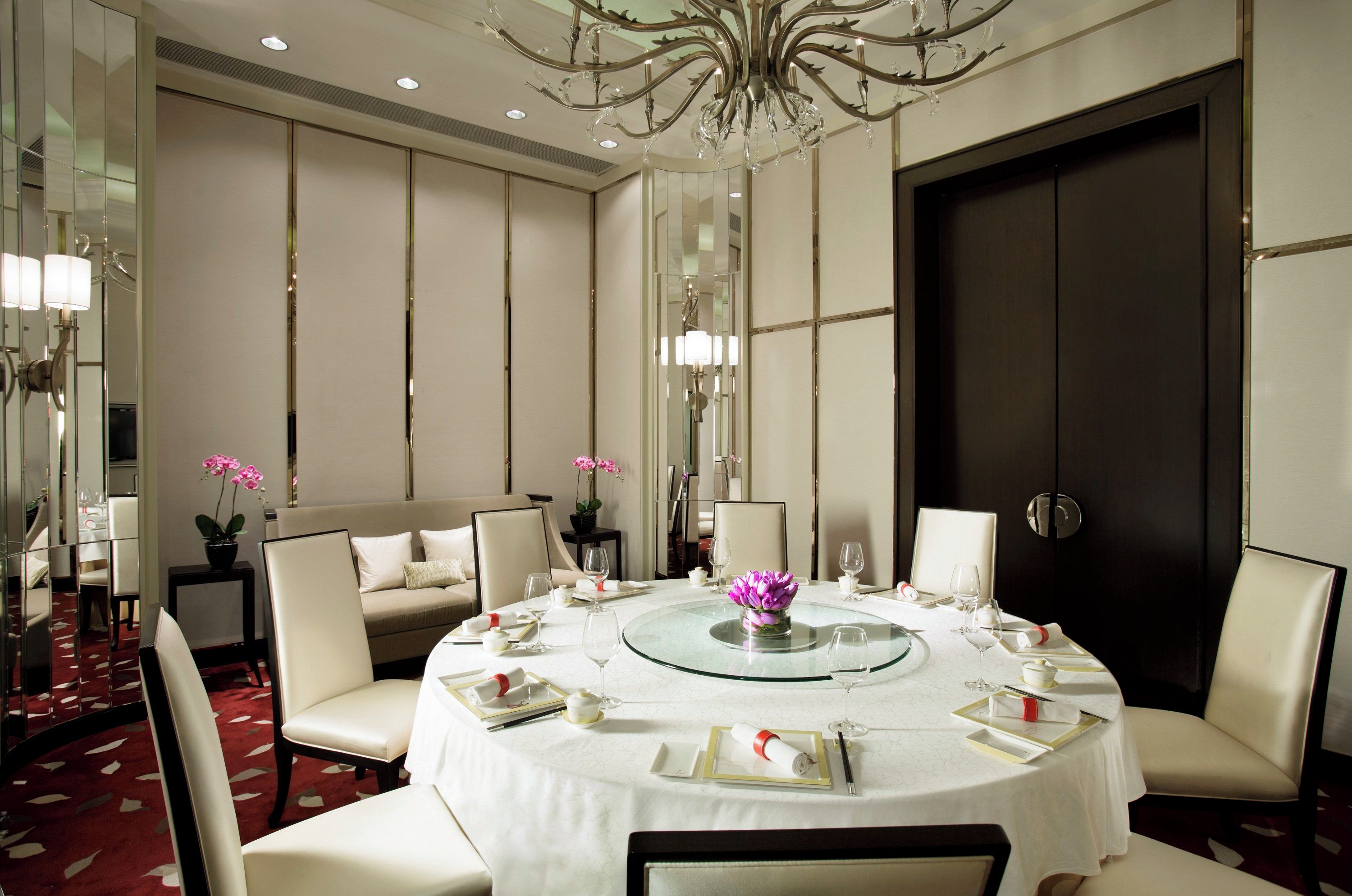 A formal dining room with a round table, white chairs, and a large mirror.
