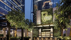 A modern bar with a glass facade, surrounded by large potted plants and a seating area with chairs. - The Langham, Shenzhen (Shenzhen)