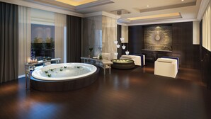 Una habitación de hotel moderna con una bañera de hidromasaje circular grande, una zona de estar con sofá y sillones, y una obra de arte de gran tamaño colgada en la pared.