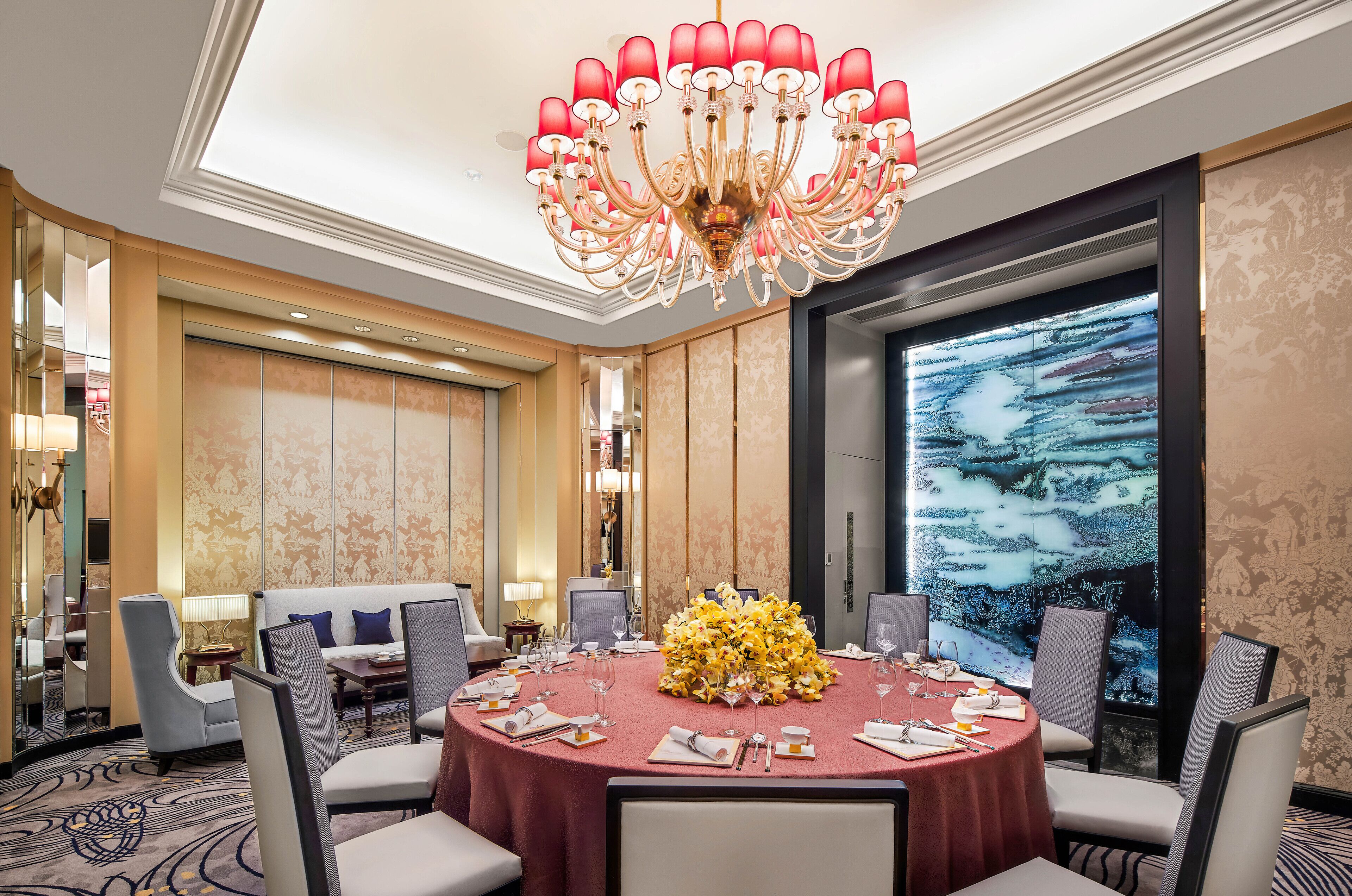 A dining area with a round table, chairs, a chandelier, and a large window with a view.