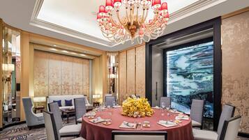 A dining area with a round table, chairs, a chandelier, and a large window with a view.