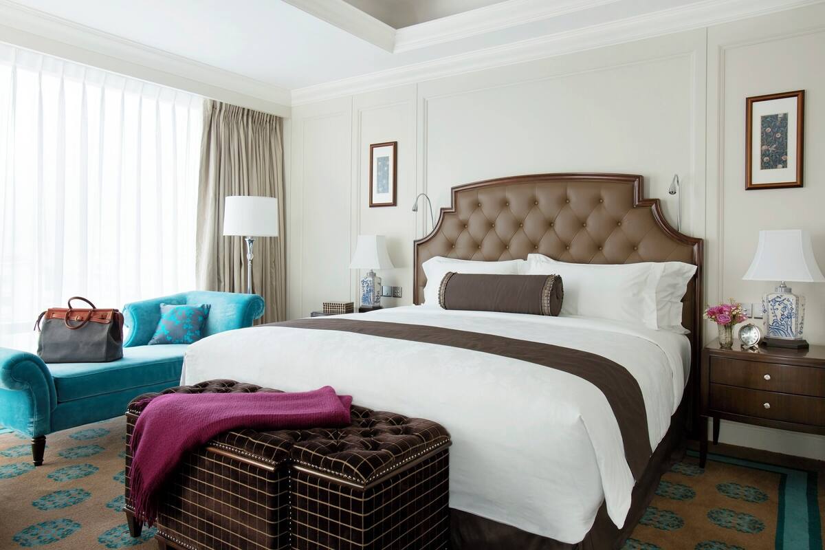 Ein Hotelzimmer mit einem großen Bett, einem blauen Sessel, einem Nachttisch aus Holz und einer dekorativen Lampe.