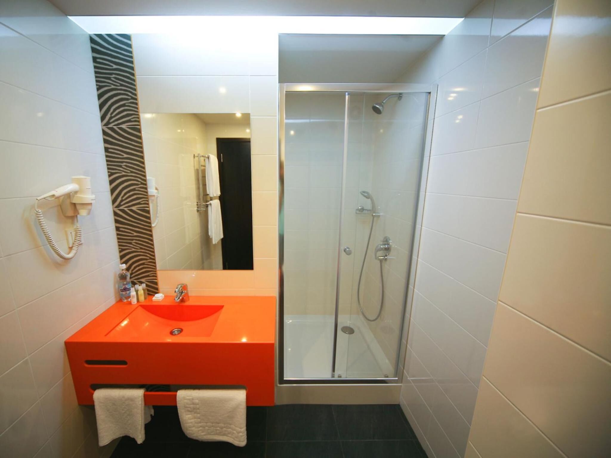 Un baño moderno con ducha envuelta en vidrio, un lavabo rojo y un espejo con estampado de cebra.