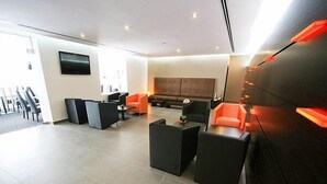 Un hall d’hôtel moderne doté d’un espace salon, d’un téléviseur à écran plat fixé au mur et d’un comptoir d’accueil.