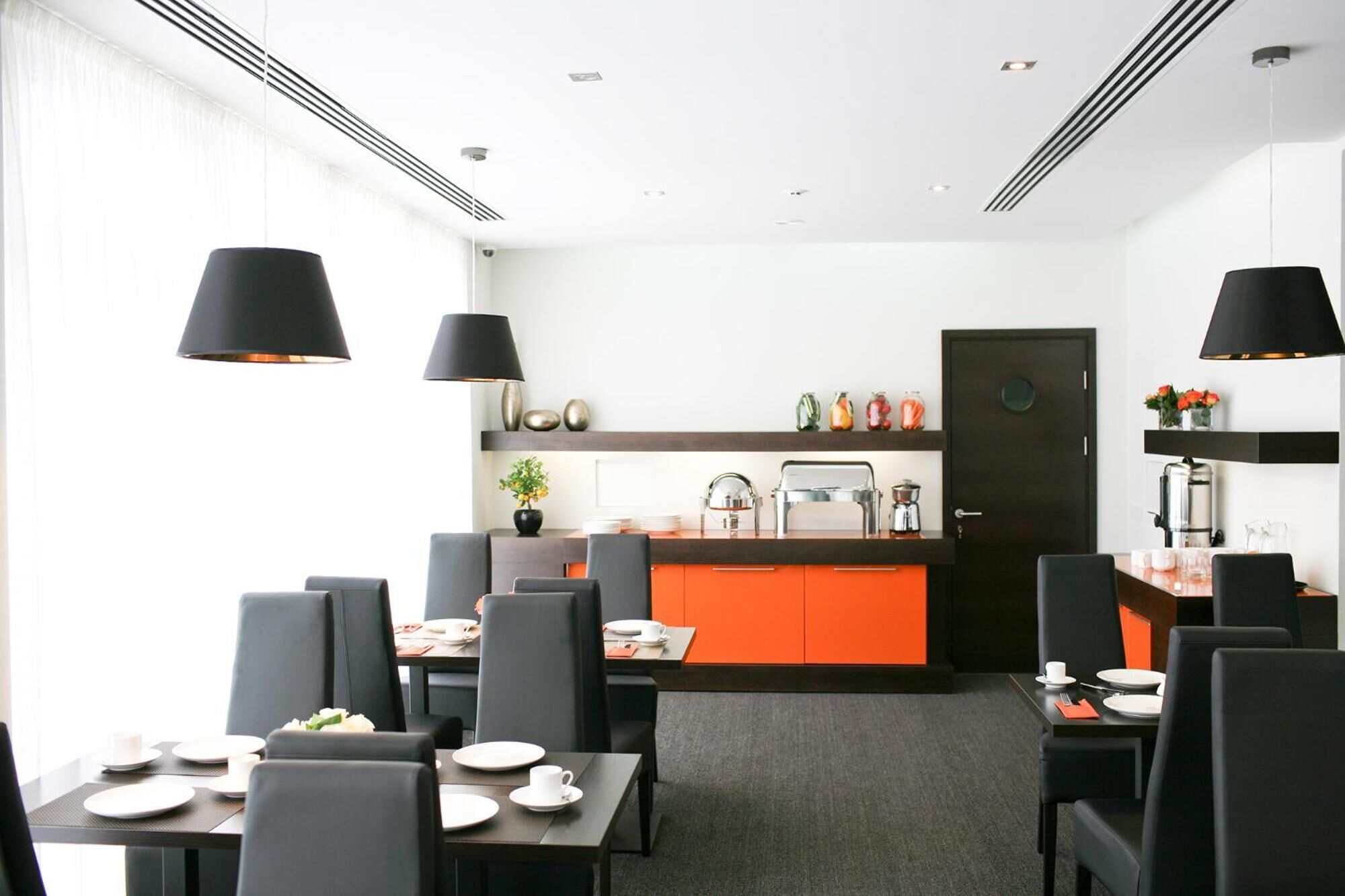 A modern dining area with black chairs, a central orange counter, and black pendant lights.