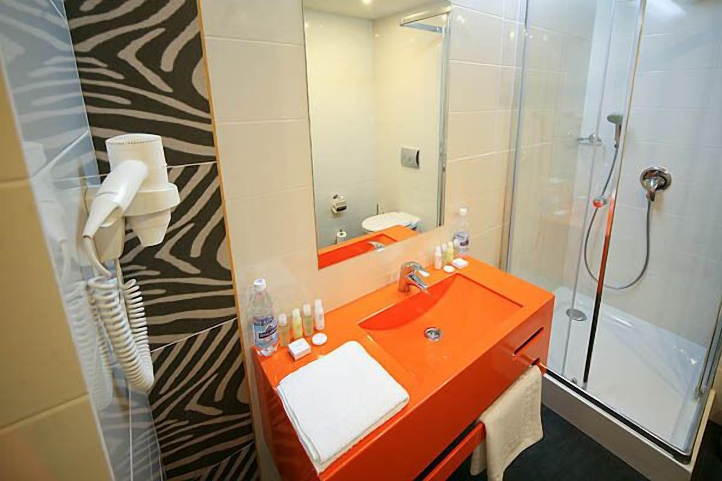 A bathroom with a zebra-patterned wall, an orange sink, a glass shower enclosure, and a white towel on the sink.
