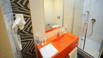 A bathroom with a zebra-patterned wall, an orange sink, a glass shower enclosure, and a white towel on the sink.