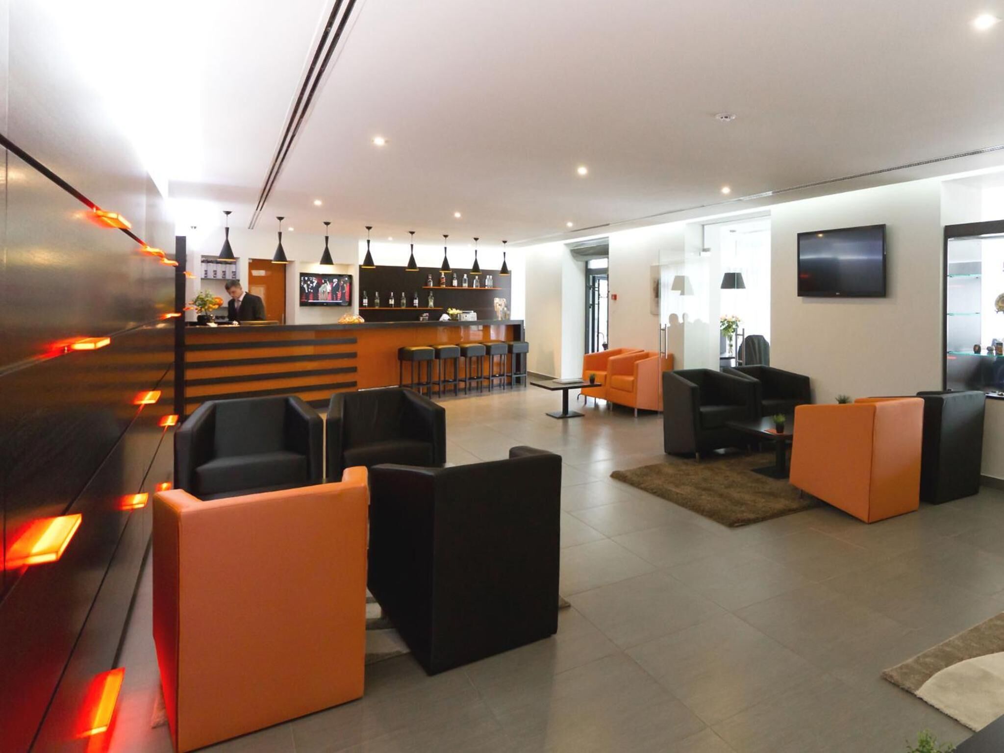 A modern lobby with a bar area, seating arrangements, and a television mounted on the wall.