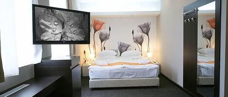 A hotel room with a bed, a television, a large mirror, and artwork on the walls.