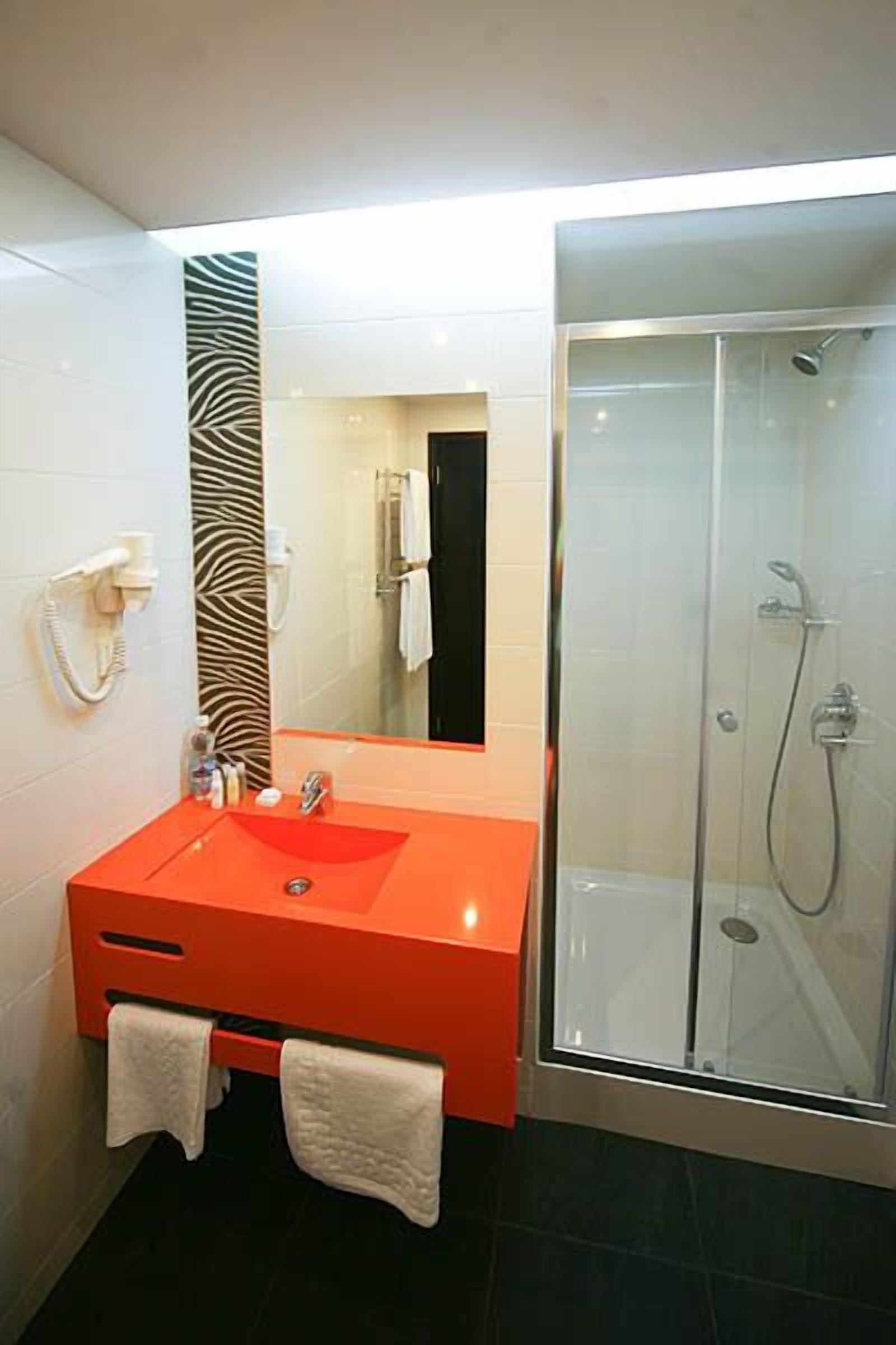 A bathroom with a red sink, a glass shower enclosure, and a mirror with a zebra pattern wall.