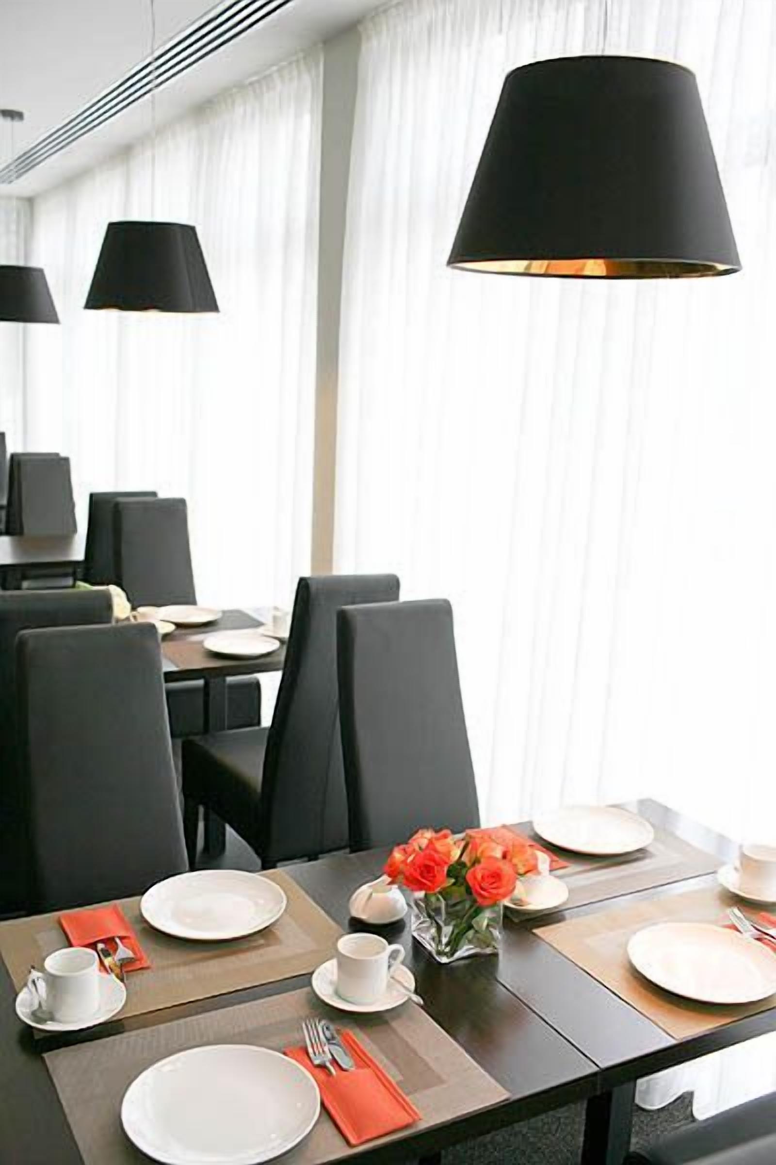 A dining area with black chairs, white plates, and a vase of orange flowers.