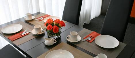 Une table à manger dressée avec des assiettes, des couverts et un vase rempli de roses rouges.