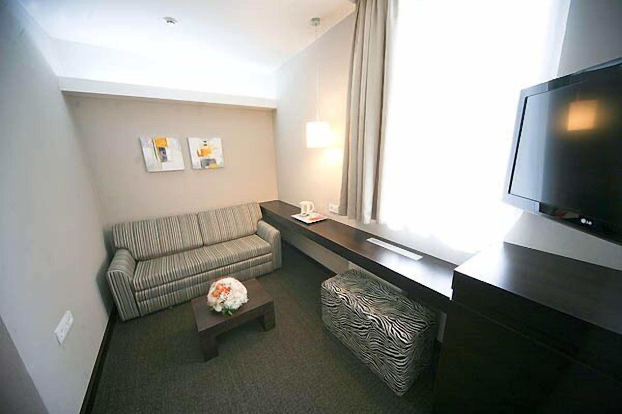 Una habitación de hotel moderna con un sofá, una mesita con un ramo de flores, un reposapiés estampado de cebra, un televisor de pantalla plana y una obra de arte en la pared.