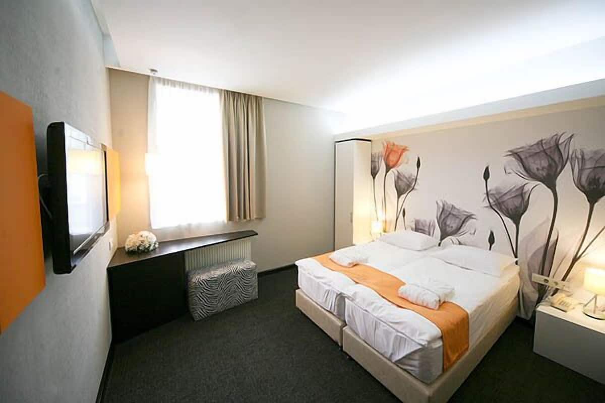 A hotel room with a bed, a desk, a chair, a lamp, and a painting on the wall.