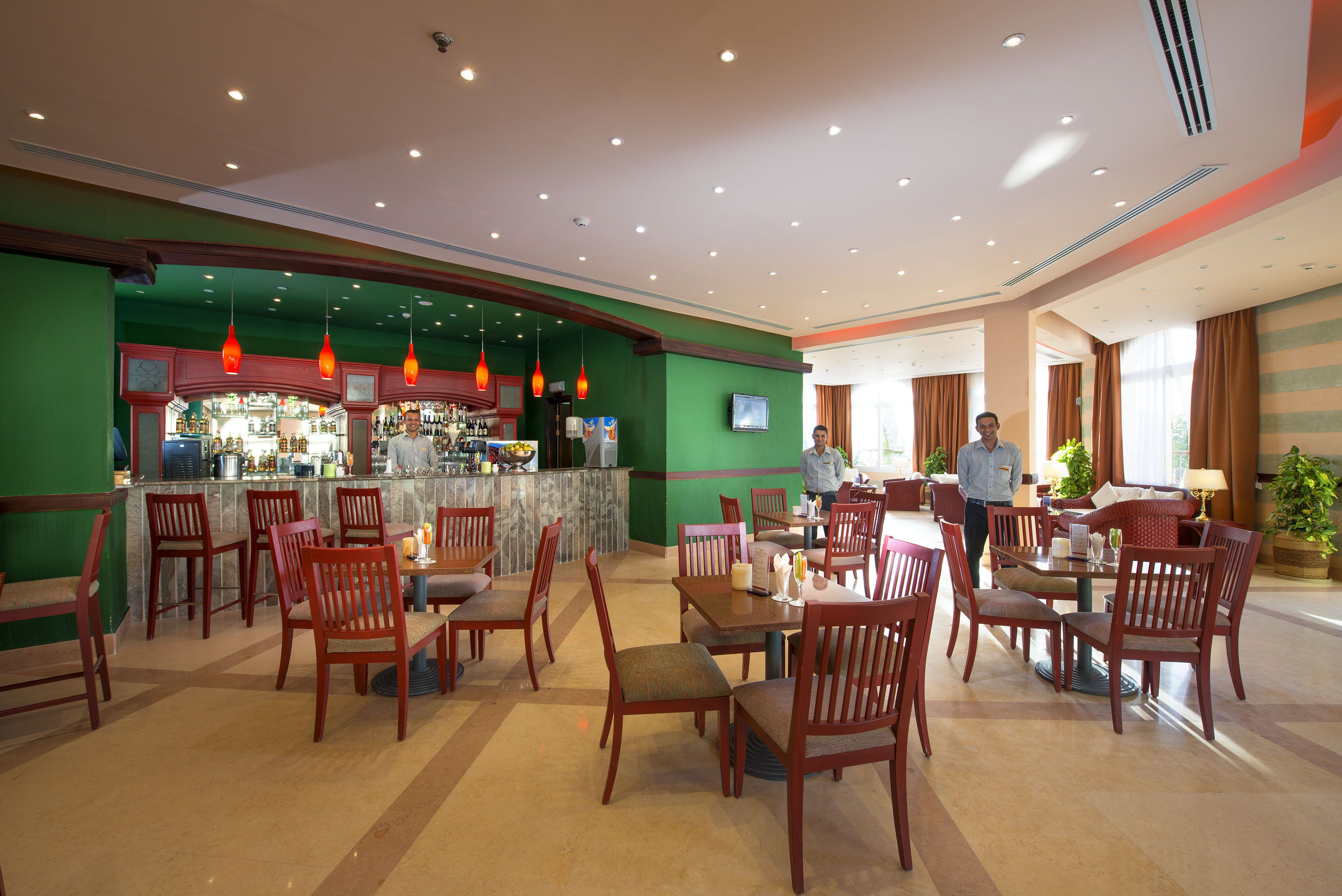 A hotel lobby with a bar area, multiple dining tables, and chairs.