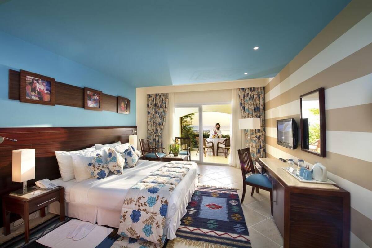 A hotel room with a bed, a desk, a TV, and a balcony with a table and chairs.