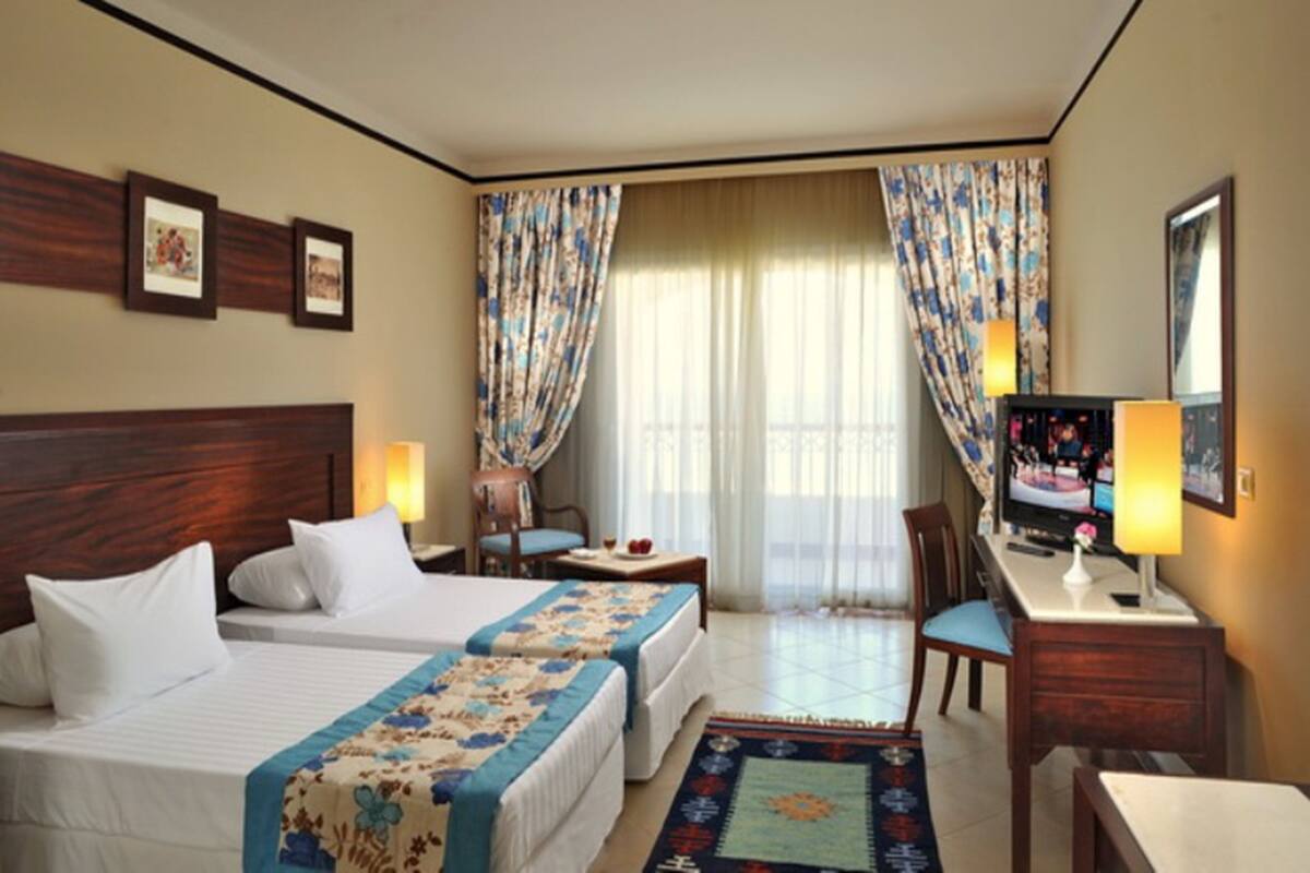 A hotel room with two beds, a desk, a chair, a TV, and curtains.