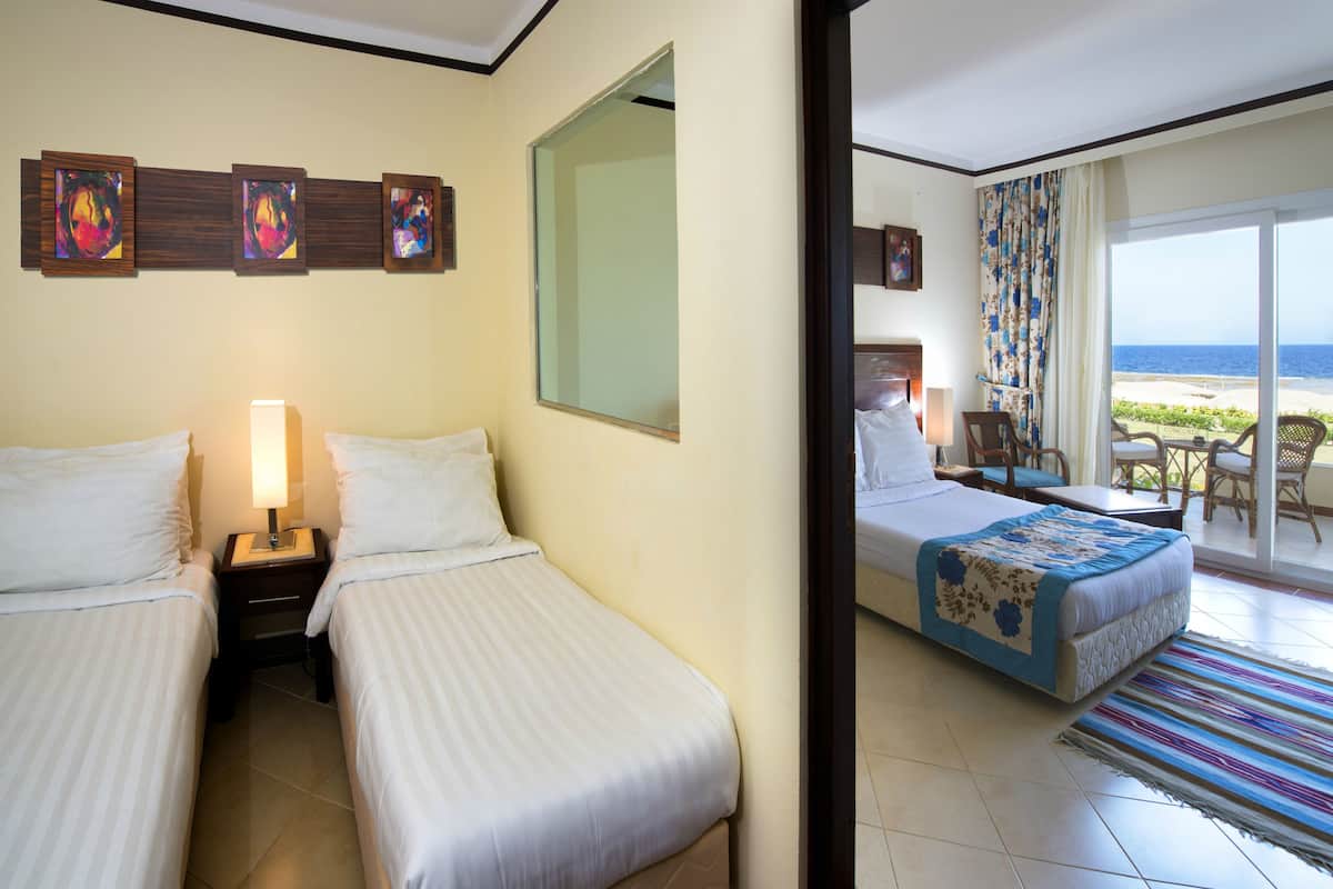 A hotel room with two beds, a large mirror, and a view of the beach through the sliding glass door.