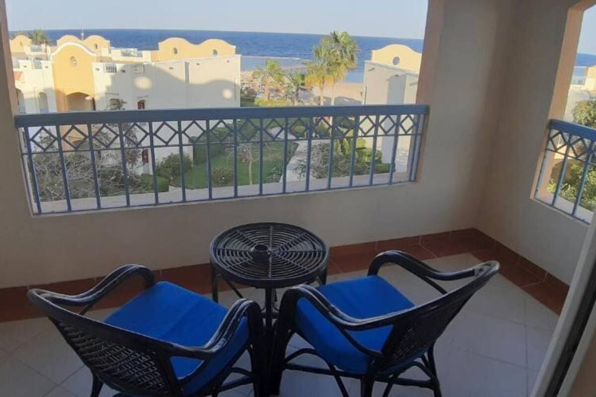 A balcony with a table and chairs, a view of buildings and palm trees, and a clear sky.