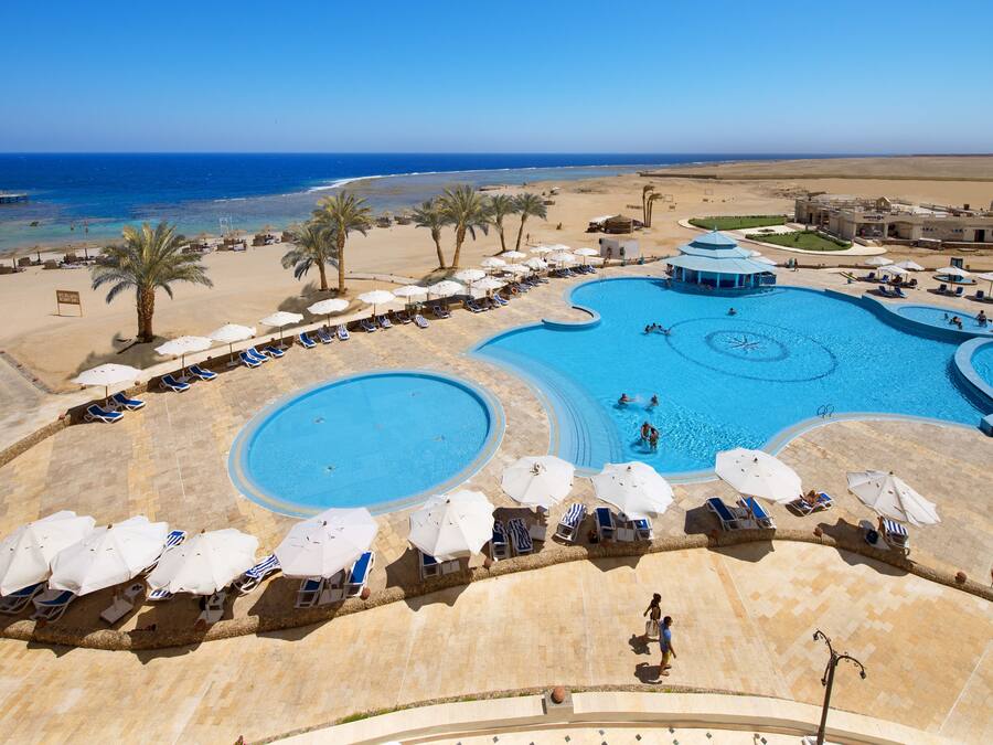 Un resort con una piscina grande, tumbonas, sombrillas y vistas a la playa y al océano.