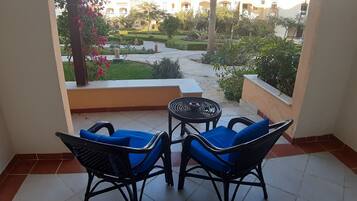 A balcony with two blue cushioned chairs and a small round table, overlooking a well-maintained garden with pathways and various plants.