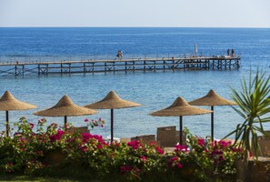 A pier extending into the sea with beach umbrellas and lounge chairs in the foreground. - Concorde Moreen Beach Resort & Spa (Marsa Alam)