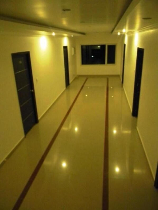 A long, narrow hallway with a shiny floor and a door on the left. - Hotel Pong View (Dharamshala)