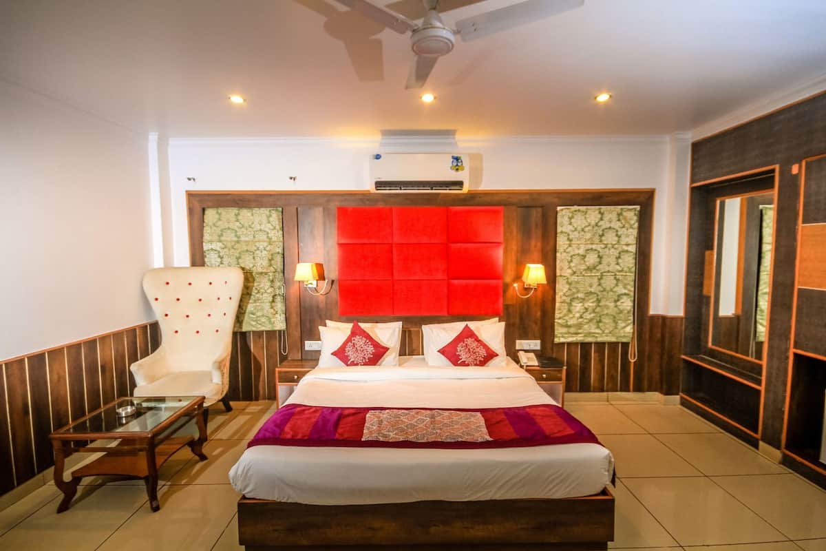 A hotel room with a bed, a chair, a nightstand, and an air conditioning unit.