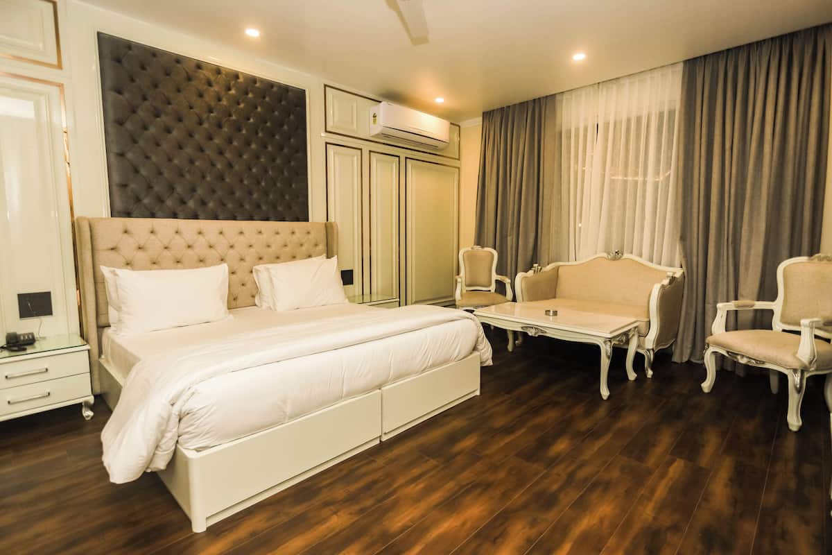 A hotel room with a large bed, a seating area with two chairs, a small table, and a wardrobe.