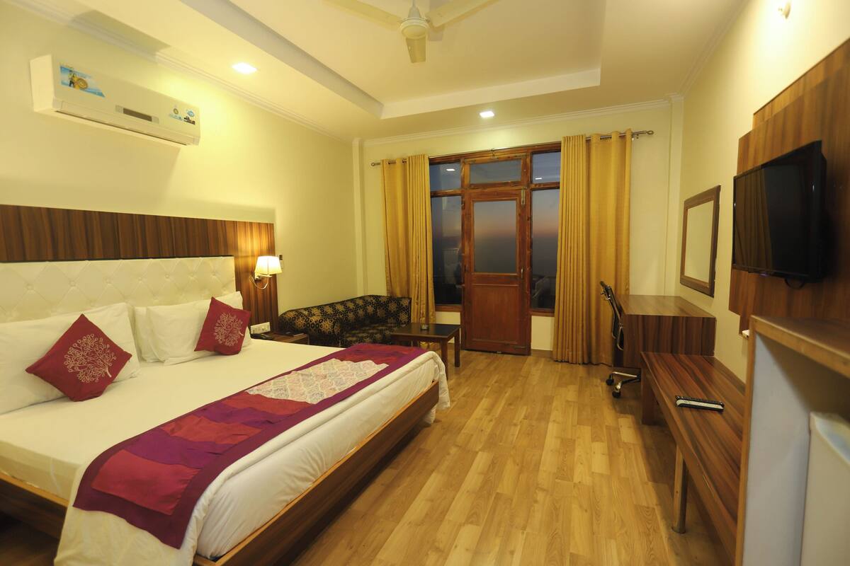 A hotel room with a bed, a desk, a television, and a window with curtains.