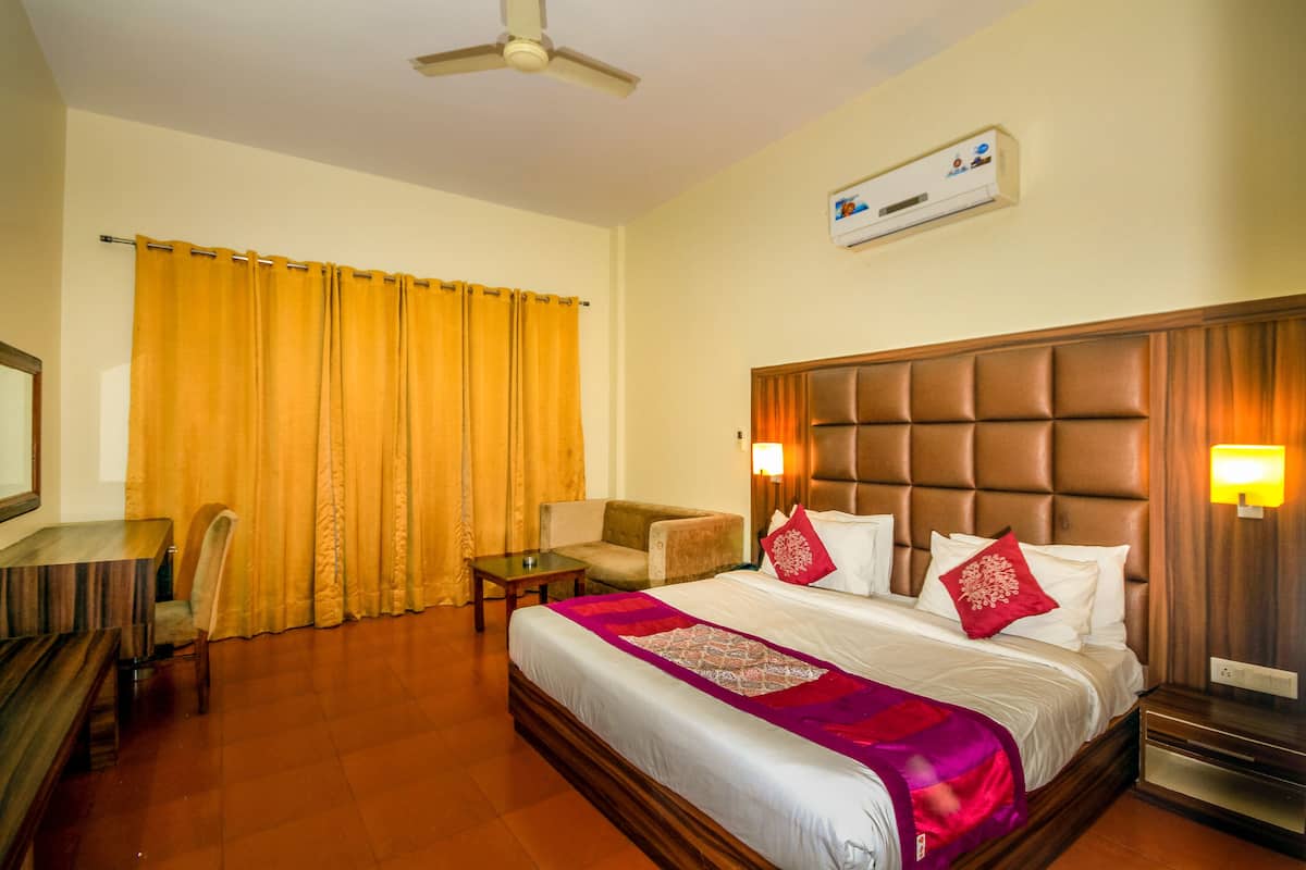 A hotel room with a large bed, a wooden headboard, a desk, a chair, a small table, and a ceiling fan.