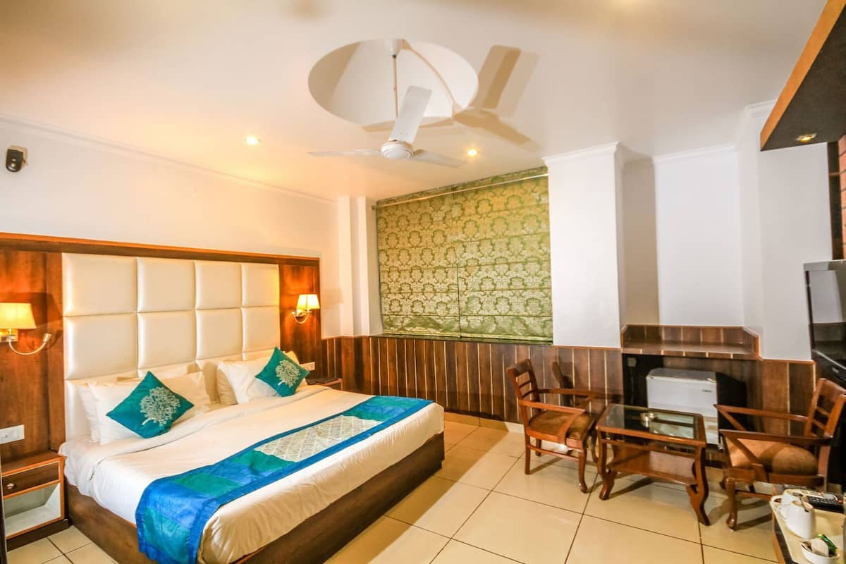A hotel room with a bed, a desk, a chair, a ceiling fan, and a TV.