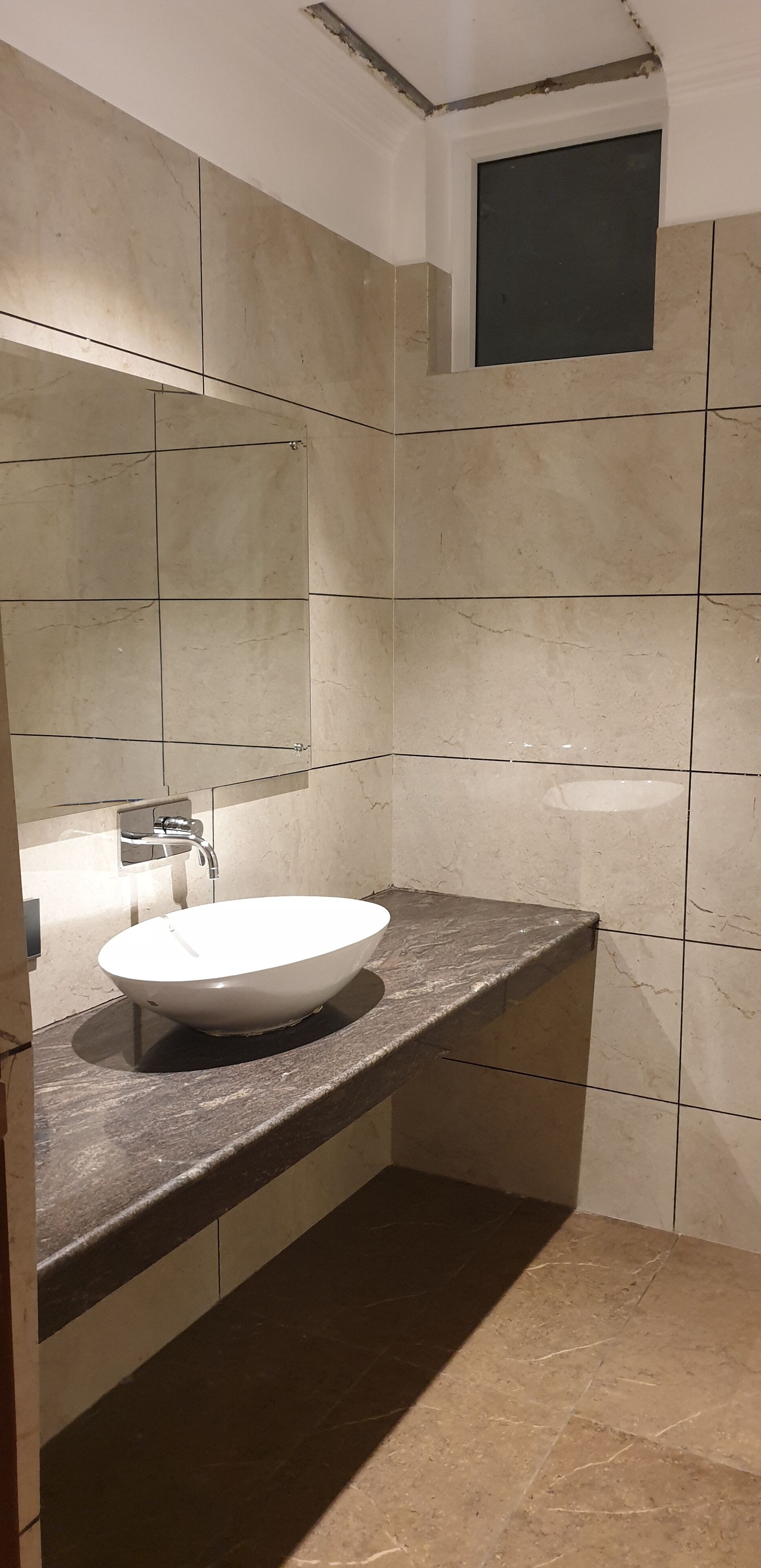 A bathroom with a white sink, dark countertop, and beige tiled walls.