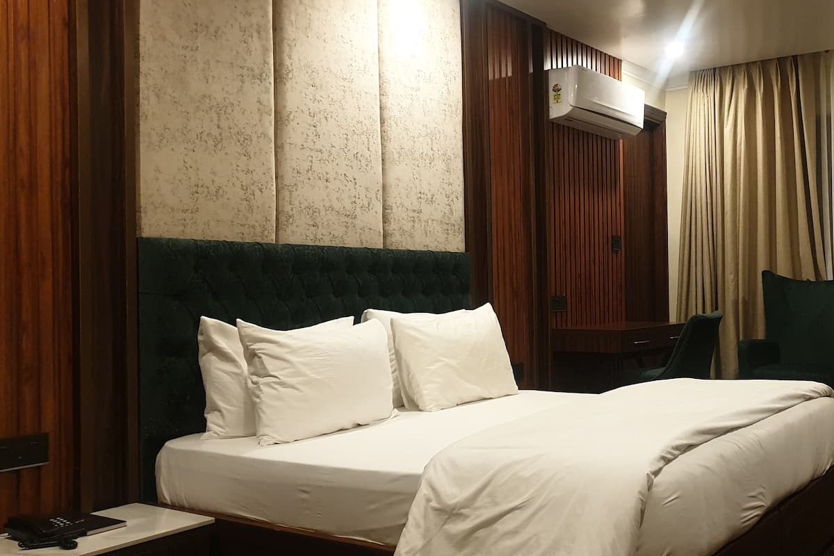 A hotel room with a large bed, a desk, and a chair. There is an air conditioning unit on the wall.