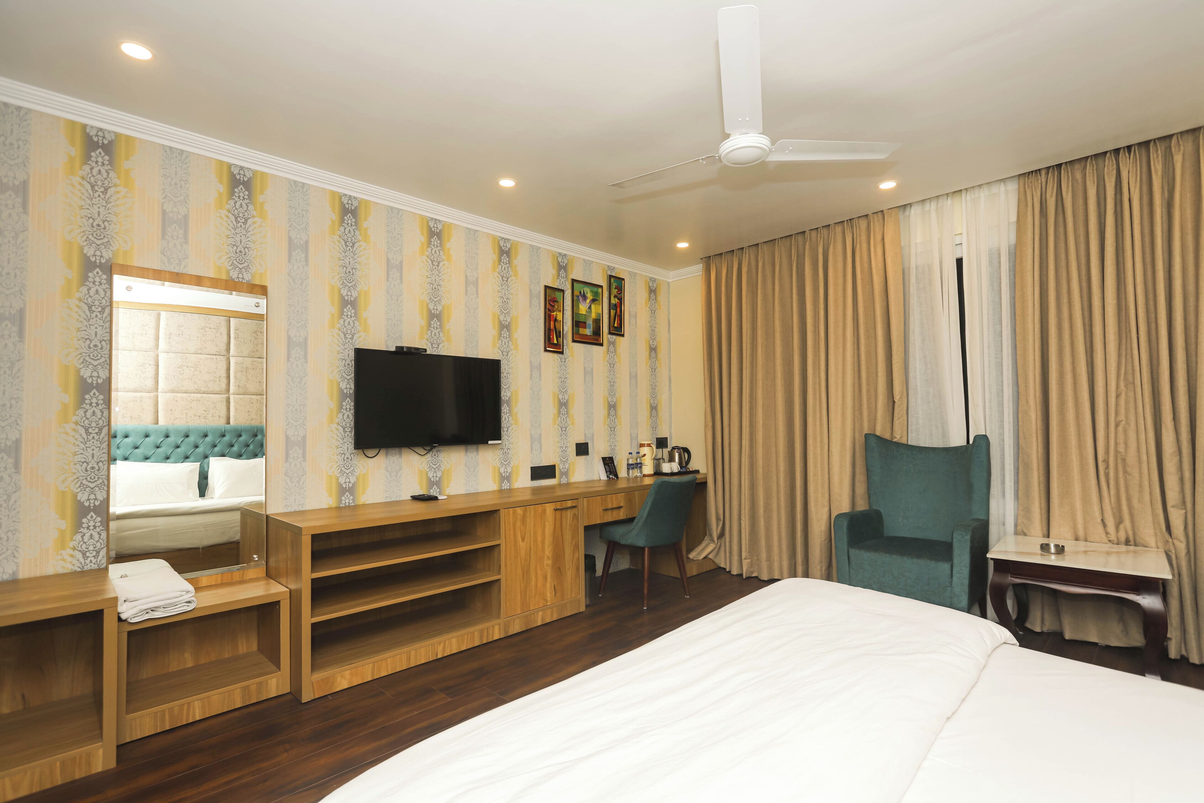 Una habitación de hotel con cama, escritorio, silla, televisor y ventilador de techo.