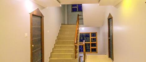 A spacious interior with a central staircase, a tiled floor, and a door on the left.