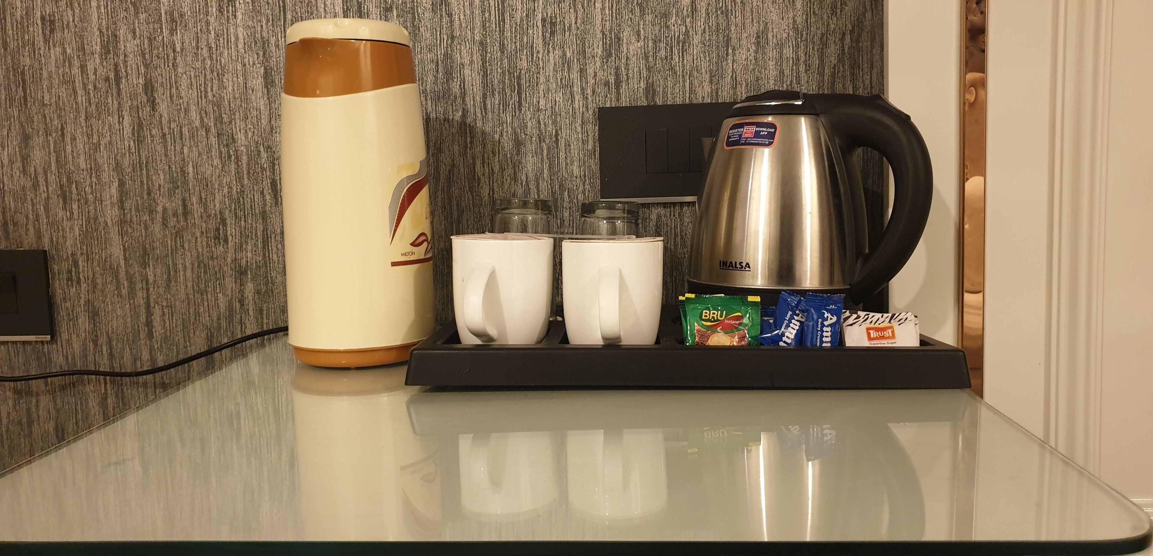 A kitchen counter with a coffee maker, a water bottle, two cups, and a tray with tea bags.