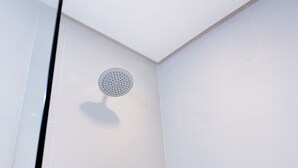 A modern shower with a round, perforated head in a corner of a room with white tiled walls. - Red Planet Makati Avenue Manila (Makati)
