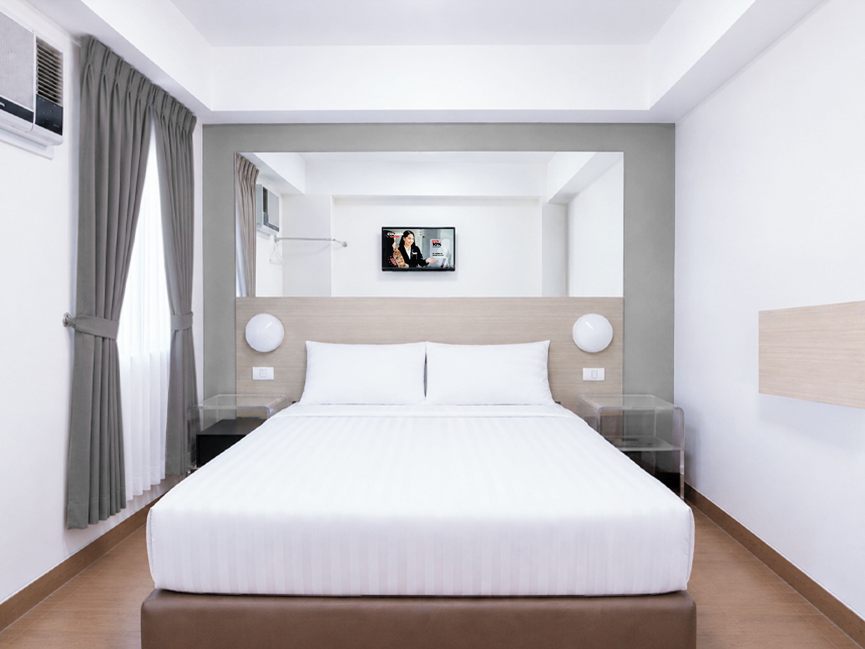 Una habitación de hotel moderna con una cama grande, mesitas de noche, un televisor y un espejo.