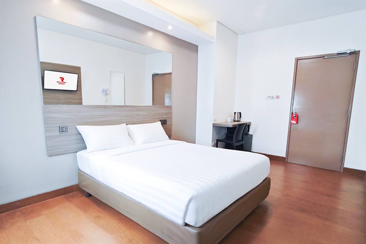 Una habitación de hotel con una cama, un escritorio, una silla, un espejo y una puerta.