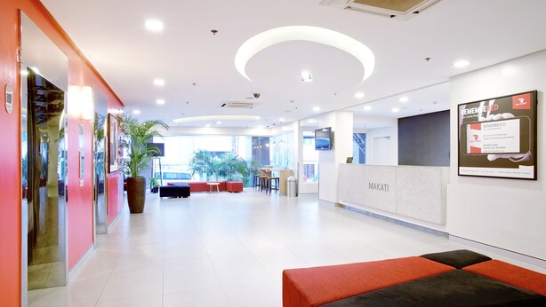 A modern lobby with a reception desk, seating area, and a large potted plant. - Red Planet Makati Avenue Manila (Makati)