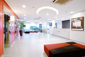 A modern lobby with a reception desk, seating area, and a large potted plant. - Red Planet Makati Avenue Manila (Makati)