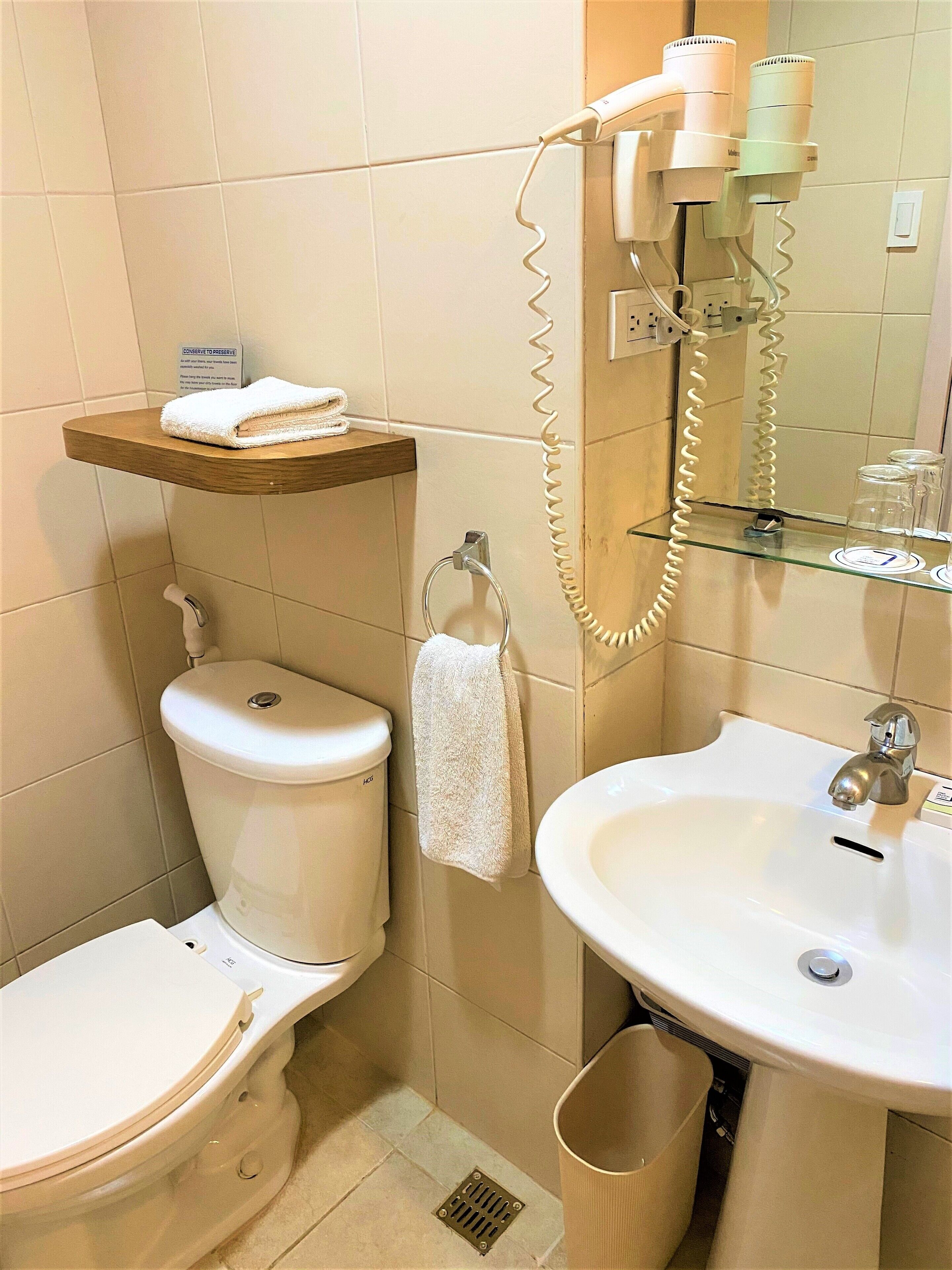A bathroom with a toilet, sink, towel rack, and a hairdryer mounted on the wall.