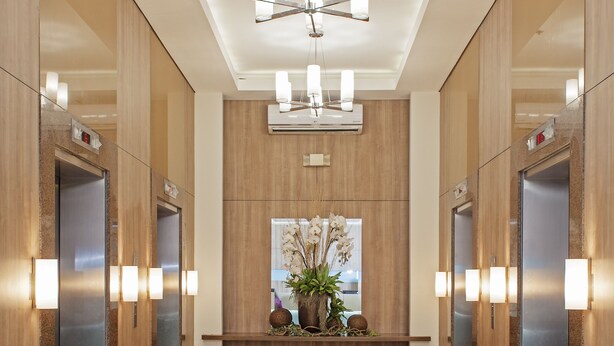 A modern elevator lobby with a central reception desk, wooden paneling, and a chandelier. - One Pacific Place Serviced Residences (Makati)