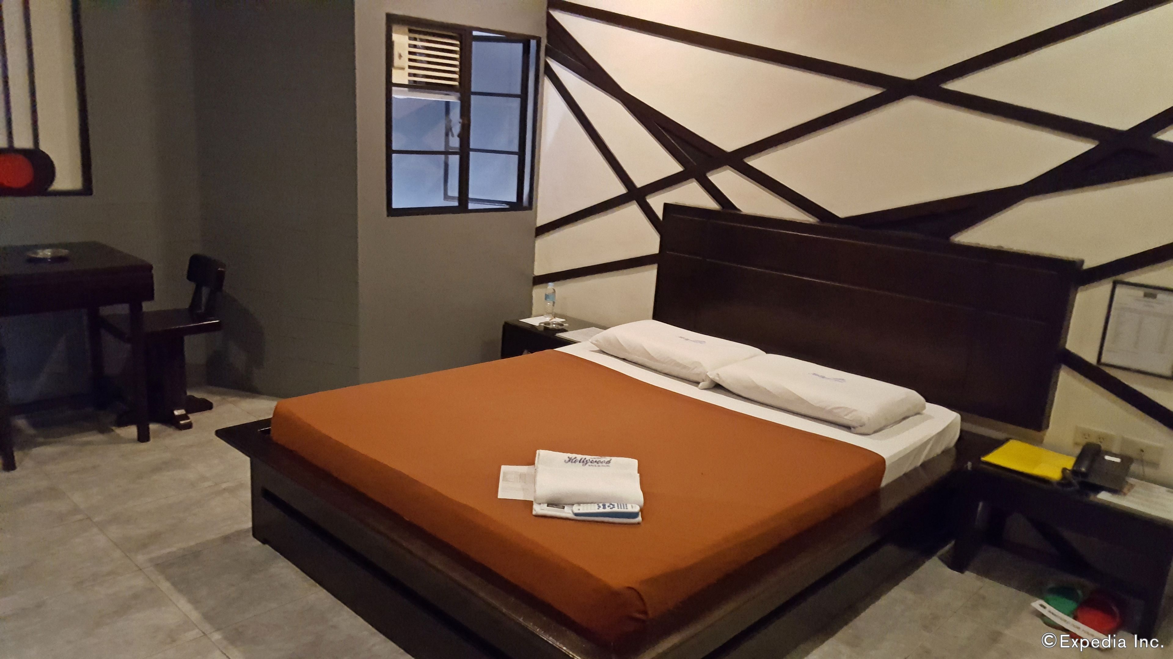 A hotel room with a large bed, a desk, a chair, a nightstand, and a window with blinds.